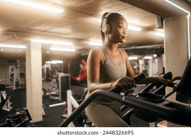 A dedicated african american sportswoman with headphones is doing workouts on stair climbing machine at gym. - Powered by Shutterstock