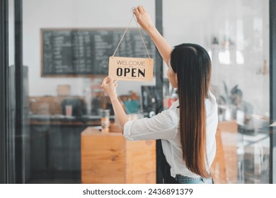 A dedicated cafe owner hangs an inviting 'Welcome Open sign, signaling the start of the day in her cozy coffee shop, an emblem of small business hospitality and readiness. - Powered by Shutterstock