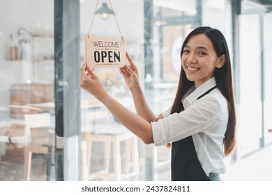 A dedicated cafe owner hangs an inviting "Welcome Open sign", signaling the start of the day in her cozy coffee shop, an emblem of small business hospitality and readiness. - Powered by Shutterstock