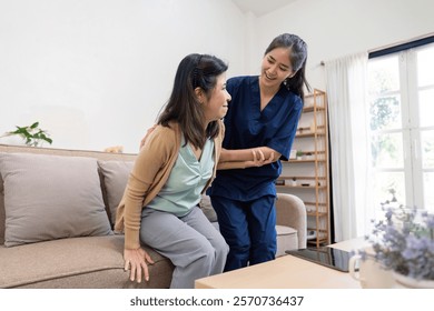 Dedicated caregiver assisting elderly client as she stands up from the sofa during a home care visit