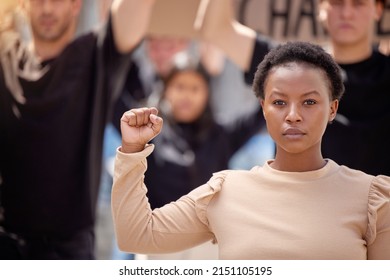 Dedicated To The Cause. Shot Of A Young Woman With Her Fist Raised In Solidarity At A March.