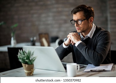 Dedicated entrepreneur sitting at office desk and reading an e-mail while working on a computer. 