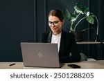 A dedicated European businesswoman works on her laptop in a modern office, exemplifying confidence and productivity. Perfect for themes of professionalism, focus, and successful business management.