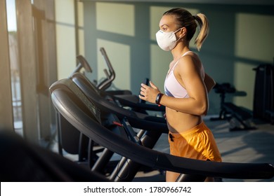 Dedicated female athlete jogging on running track while wearing protective face mask in a gym during coronavirus epidemic. 