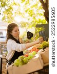 Dedicated female merchant putting price tags on freshly harvested seasonal produce, ready for selling at farmers market. Woman vendor preparing locally grown food products for customers.