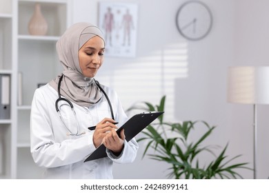 A dedicated female Muslim doctor in a hijab and white coat is focused on patients' reports while working in a clinic. - Powered by Shutterstock