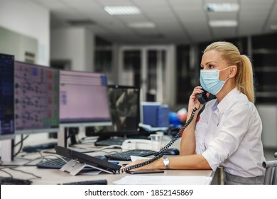 Dedicated Hardworking Blond Female Boss In Suit With Face Mask On Sitting In Control Room In Heating Plant And Having Important Phone Conversation During Corona Virus Outbreak.