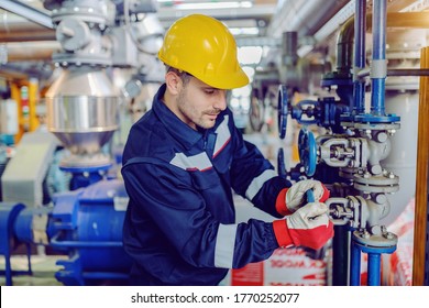 Dedicated hardworking worker in protective working clothes and with helmet on head screwing valve while standing in factory.