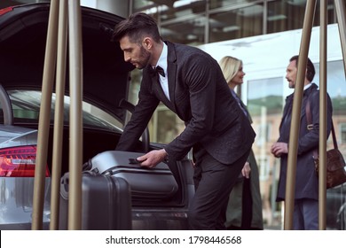 Dedicated Hotel Employee Satnding Near The Open Car Trunk Taking Out A Suitcase Helping The Guests With Luggage