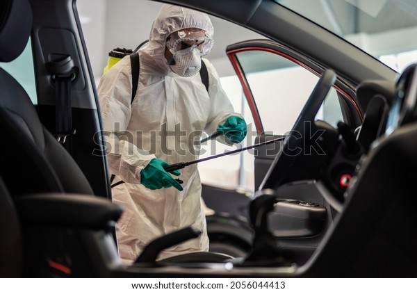 Dedicated male expert in\
white protective uniform with mask and goggle disinfection (car\
salon) with antiseptic sprayer. He cleaned the interior of the car.\
Coronavirus