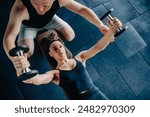 A dedicated male personal trainer acts as a coach, guiding a woman in lifting a dumbbell at the gym. Personal Training Male Trainer Assists Woman in Dumbbell Lift at the Gym