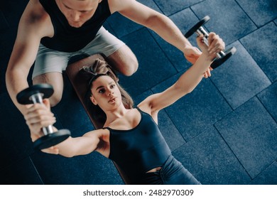 A dedicated male personal trainer acts as a coach, guiding a woman in lifting a dumbbell at the gym. Personal Training Male Trainer Assists Woman in Dumbbell Lift at the Gym - Powered by Shutterstock