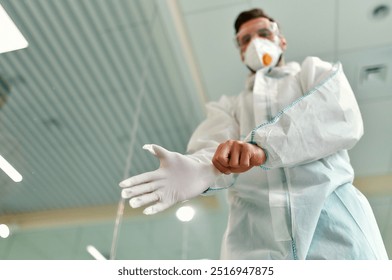 A dedicated medical professional, fully in protective gear, is carefully preparing to put on gloves to maintain the highest safety and hygiene standards in a clinical healthcare setting - Powered by Shutterstock