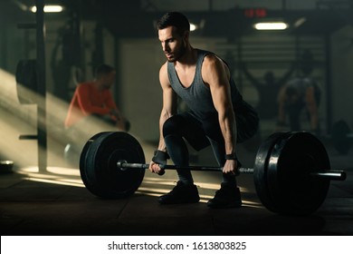 Dedicated sportsman practicing deadlift with barbell during sports training in a gym. There are people in the background. 