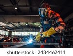 Dedicated young worker welding a piece of metal while assembling a metal construction for his project. Wearing safety equipment, gloves and a mask while working with great precision. Copy space.