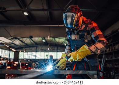 Dedicated young worker welding a piece of metal while assembling a metal construction for his project. Wearing safety equipment, gloves and a mask while working with great precision. Copy space. - Powered by Shutterstock