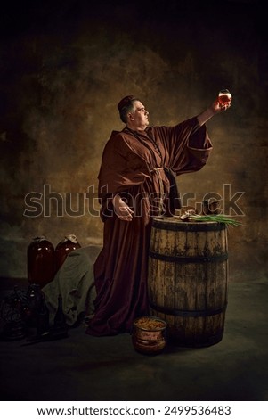Dedication to abbey brewing through the ages. Medieval monk raising glass with freshly brewed ale, beer against stage background. Concept of comparison of eras, history, brewery, traditions