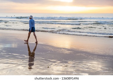 Dee Why Beach, NSW / Australia - March 20th 2019: An Old Australian Retiree Wearing A White Cowboy Hat Is Walking On The Beach At Sunrise