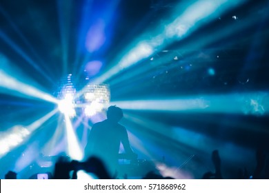 Deejay silhouette on a stage with big disco ball at background with the colorful rays on it