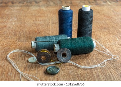 Deep blue, green, black and gray colored sewing thread spools with needle, measuring tape and sewing accessories on brown wooden background. - Powered by Shutterstock