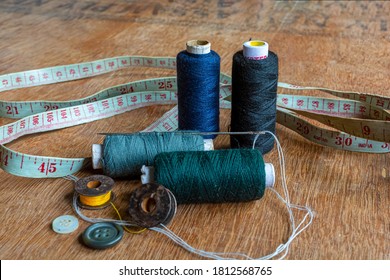 Deep blue, green, black and gray colored sewing thread spools with needle, measuring tape and sewing accessories on brown wooden background. - Powered by Shutterstock