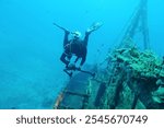 Deep blue ocean with underwater photographer and old shipwreck. Sunken boat, remains in the ocean. Scuba diving adventure trip. Marine life, wreck and diver. Travel photo, diver and seascape.