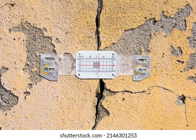 Deep crack in a damaged old plaster wall with plastic mechanical crack meter designed to measure movement across surface cracks and joints
