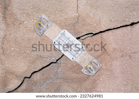 Deep crack in a damaged old plaster wall cause due to subsidence of foundations structural failures with plastic mechanical crack meter designed to measure movement across surface cracks and joints