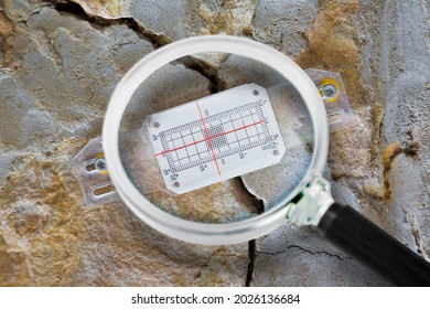 Deep crack in a damaged old stone wall cause due to subsidence of foundations structural failures with plastic mechanical crack meter designed to measure movement across surface cracks and joints