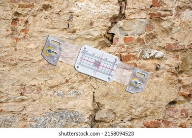 Deep crack in a damaged old stone wall cause due to subsidence of foundations structural failures with plastic mechanical crack meter designed to measure movement across surface cracks and joints