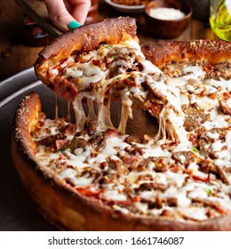 Deep Dish Meat Pizza On A Wooden Table With A Slice Being Pulled