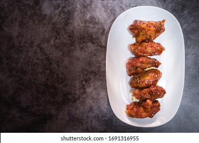 Der tiefgefrorene Hühnerflügel mit scharfer Sauce im koreanischen Stil wird auf weißem Teller serviert. Draufsicht mit freiem Platz für Ihren Text auf rustikalem Hintergrund.