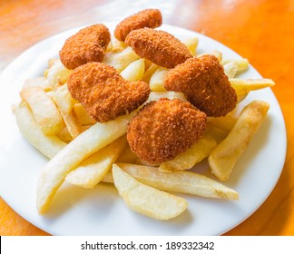 The Deep Fried Potato Chips And Chicken Nuggets On The White Dish With The Wooden Table