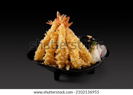 Deep fried Shrimps Tempura,traditional japanese food served with sliced radishes and a cup of dipping sauce on darkgrey background.