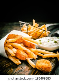 Deep fried takeaway crumbed fish portions and golden potato chips served in a disposable paper cone with tartar sauce on an old wooden table in a restaurant or fish shop