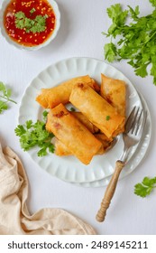 Deep fried vegetable spring rolls or egg rolls and sauce , Thai called popia, in white plate on a white table background with fork, top view food table