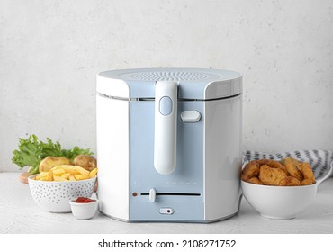 Deep fryer with bowls of delicious fast food and vegetables on table - Shutterstock ID 2108271752