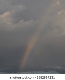 Deep gray clouds part as a radiant rainbow fills the sky, adding light and magic to a dramatic weather scene.