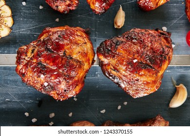 Deep Grilled Hot And Spicy Bbq Chicken Thighs On A Skewer Top View. Macro Photo Of Appetizing Barbecue Poultry Legs With Spices, Tomatoes, Garlic, Salt On Black Blur Background