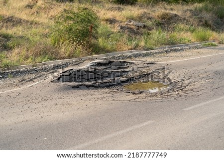 Deep hole in the road. Deformed asphalt surface with potholes melts from heat due to heavy overloaded trucks driving at hot summer days. 
