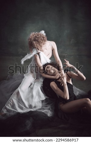 Deep love and salvation. Portrait of two women, angel and demon against dark, green, vintage background. Making choice. Concept of history, remake, good and bad, creative photography