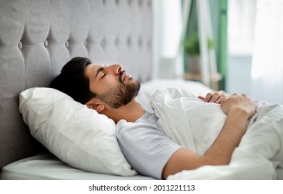 Deep male sleep. Young arab guy sleeping peacefully in his comfortable bed at home, lying with closed eyes on back. Recreation, time to rest and nap concept