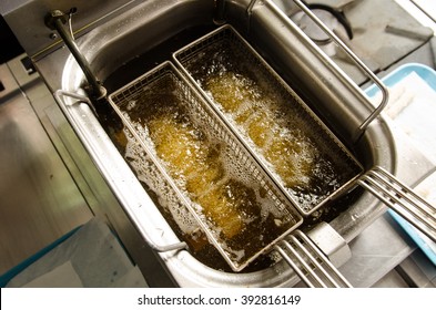 A Deep Pan Industrial Kitchen Oil Fryer, With Golden Oil, Bubbling And Frying Potatoes