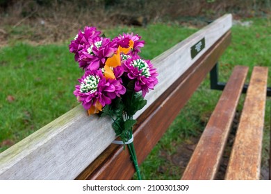 A Deep Pink Bunch Of Flowers Left On A Memorial Bench