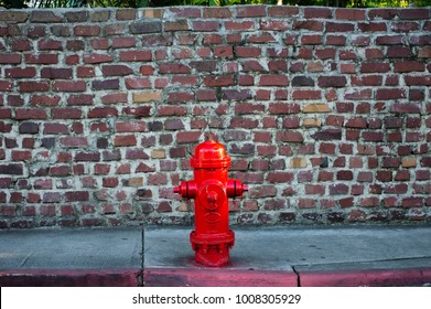 A Deep Red Fire Hydrant Sits in Front of an Old Brick Wall