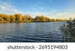 A deep river surrounded by trees and plants. Reed beds. Boats on the water. An autumn landscape in warm tones.