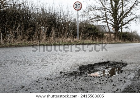 Deep road pothole filled with rainwater. Already filled once, the pot hole is a hazard to cars and other vehicles on this British rural road.