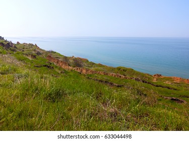 Deep sandy cliff on the background of blue sky. The destruction of the coast as a consequence of soil erosion. Landslide - threat to life.