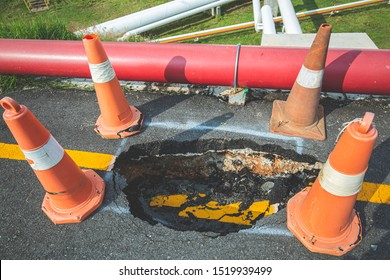Deep Sinkhole On A Street City And Orange Traffic Cone. Dangerous Hole In The Asphalt Highway. Road With Cracks. Bad Construction. Damaged Asphalt Road Collapse And Fallen
