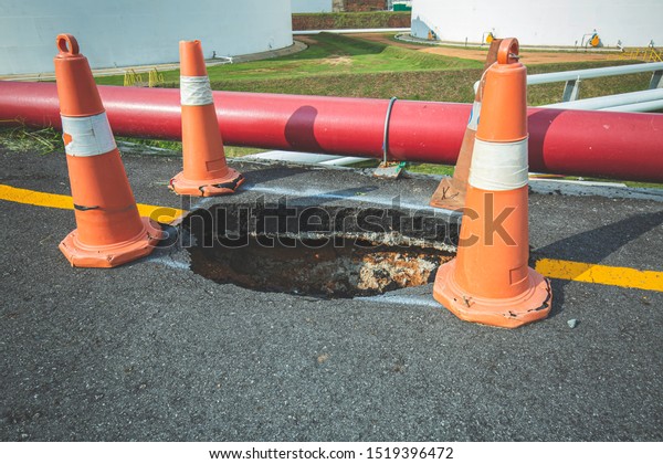 Deep sinkhole on a\
street city and orange traffic cone. Dangerous hole in the asphalt\
highway. Road with cracks. Bad construction. Damaged asphalt road\
collapse and fallen